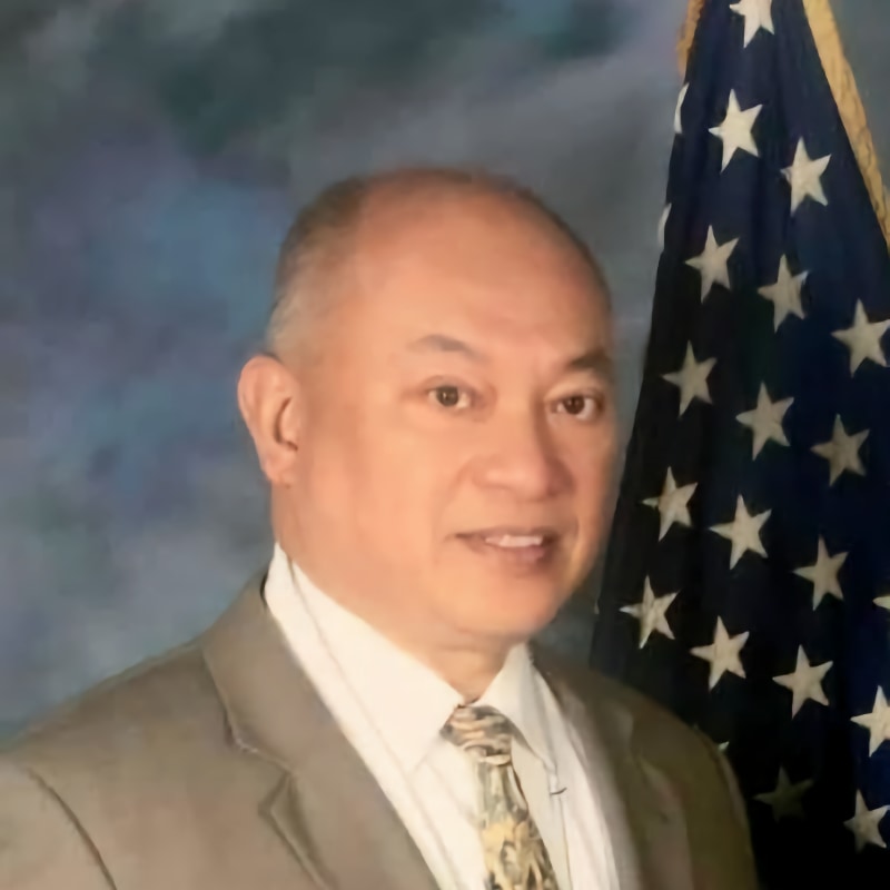 Advisory board member Philip Espina, man in tan suit standing in front of American flag